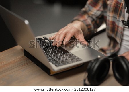 Cropped view of a man sitting at a table in front of a laptop. A man in a plaid shirt is typing on a laptop.