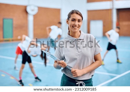 Portrait of happy physical education teacher during a class at school gym. Her students are exercising in the background.