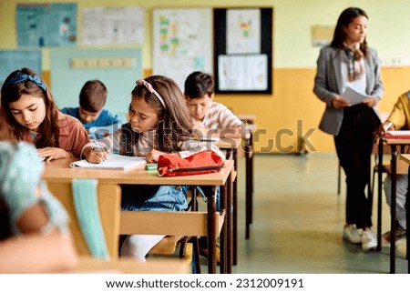 Group of elementary students having an exam at school. Focus is on Hispanic girl writing in her notebook. Royalty-Free Stock Photo #2312009191