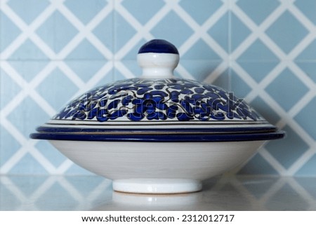 Selective focus view of pretty ceramic serving platter with blue painted cover set on shiny quartz counter with a background of blue tiles Royalty-Free Stock Photo #2312012717