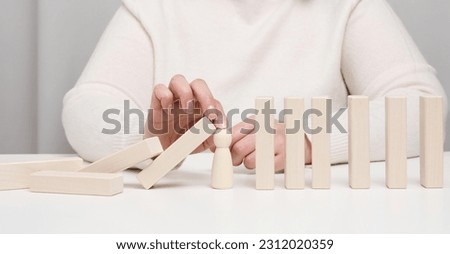 Hand stops the fall of wooden figurines of men on a white background. Concept of a strong and courageous personality capable of withstanding unequal difficulties. Strong business Royalty-Free Stock Photo #2312020359