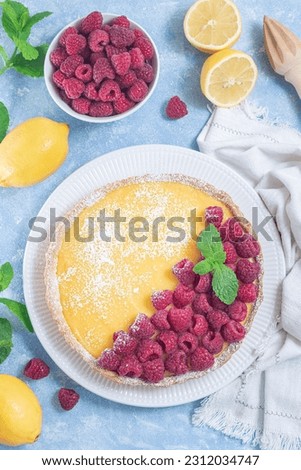 Lemon tart, garnished with fresh raspberry, icing sugar, mint, vertical top view
