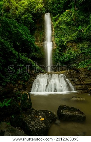 Very beautiful waterfall in the tropical rainforest of the Mentawai islands, west Sumatra, Indonesia. surrounded by tall lush trees, and clear water, perfect for adventure. Slow-speed photo. 