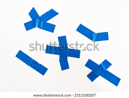 The parts of the blue adhesive plastic tape and the cross for fastening are isolated on a white background. Crumpled adhesive plastic adhesive tape for attaching photos and paper.