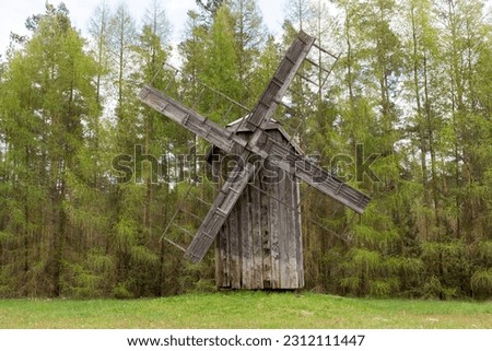 Old Wooden Windmill In Meadow, Open Air. Blades Of Mill Wooden In Rural Eastern Europe Area, Countryside. Green Forest On Background. Horizontal Landscape Plane High Quality Photo.