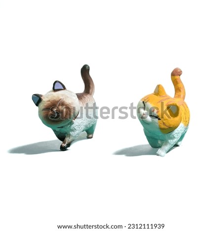 Miniature toy animals of two cats walking on a white background