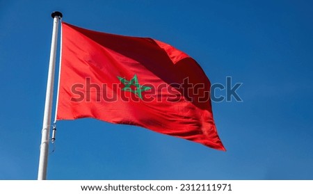 Morocco sign symbol. Moroccan national official flag on flagpole waving in the wind, blue sky background Royalty-Free Stock Photo #2312111971