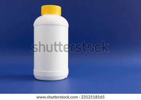 Pipe Unclogging Granules In Yellow Cap, White Plastic Bottle On Blue Purple Background. Acid Drain Cleaner, Housework Help. Horizontal Plane, Copy Space For Text.