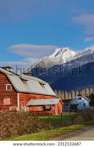 Picture of a red barn with a snowy mountain in the background off the side of the road