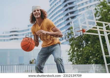 Bottom view young concentrated happy man 20s in yellow t-shirt bandana playing basketball on playground in free time walking rest relax in city outdoors on open air. Urban lifestyle leisure concept.