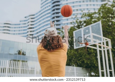 Back rear view young man 20s in yellow t-shirt bandana hold ball shooting playing basketball on playground in free time walking rest relax in city outdoors on open air. Urban lifestyle leisure concept