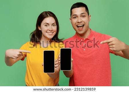 Young couple two friends family man woman wear basic t-shirt together hold use point index finger on mobile cell phone blank screen workspace area isolated on pastel plain light green color background