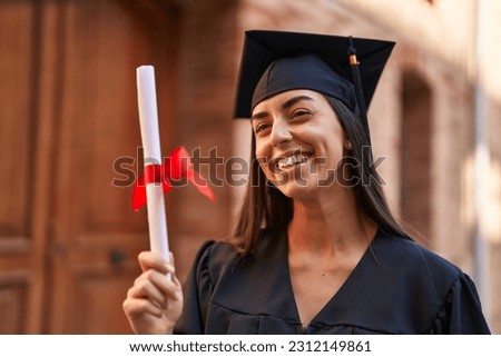 Young hispanic woman wearing graduated uniform holding diploma at university Royalty-Free Stock Photo #2312149861