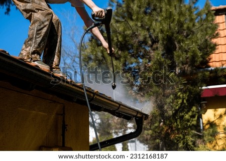 Worker standing on the roof and cleaning rain gutter with high pressure water jet. Professional with equipment for roof gutter cleaning. Maintenance and housekeeping concept of drainage channel. Royalty-Free Stock Photo #2312168187