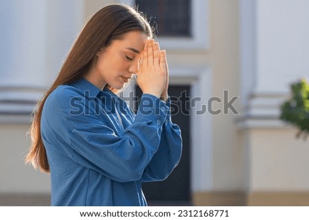 Portrait of young woman praying with closed eyes to God asking for blessing, help, forgiveness outdoors. Pretty girl clasping hands wishing luck in sunny urban city street. Town religion lifestyles Royalty-Free Stock Photo #2312168771