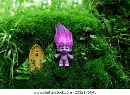 cute tale troll and little wooden door in mystery forest, natural abstract background. funny troll toy with ruffled violet hair. fairytale beautiful magic atmosphere. template for design