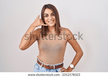 Young hispanic woman standing over white background smiling doing phone gesture with hand and fingers like talking on the telephone. communicating concepts. 