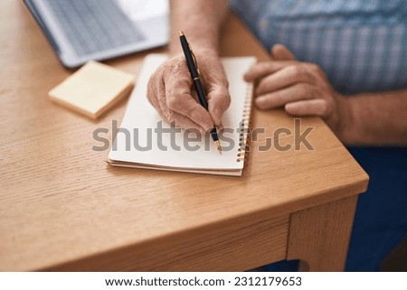 Middle age grey-haired man business worker writing on notebook at office