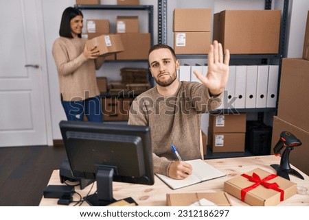 Two young people working at small business ecommerce with open hand doing stop sign with serious and confident expression, defense gesture 