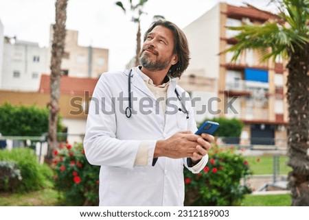 Middle age man doctor smiling confident using smartphone at park