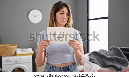 Young blonde woman asking for help holding paper at laundry room