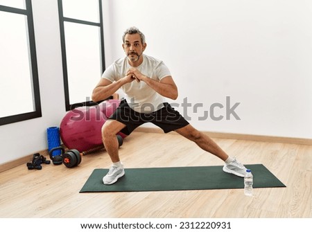 Middle age grey-haired man stretching leg at sport center