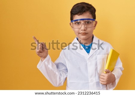 Little hispanic boy wearing scientist glasses smiling happy pointing with hand and finger to the side  Royalty-Free Stock Photo #2312236415