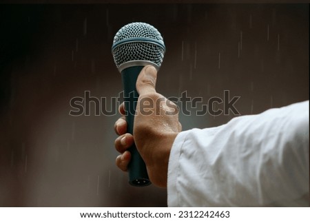 A Handheld Microphone in the hand of a black boy wearing white shirt while raining can be used as raise voice concept  newscaster media reporter