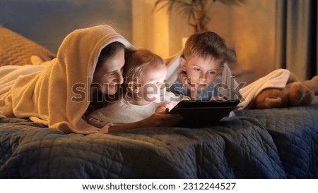 Happy family relaxing in bed with tablet computer. Family having time together, parenting, happy childhood and entertainment