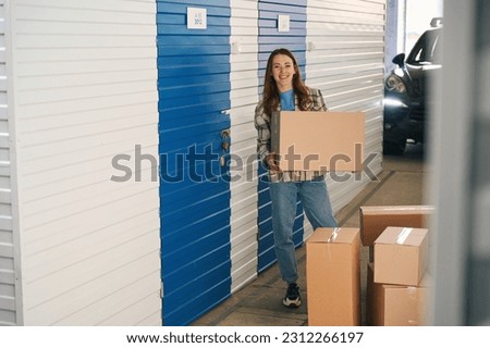 Smiling lady with many cardboard boxes near self storage unit into warehouse Royalty-Free Stock Photo #2312266197