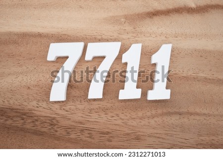 White number 7711 on a brown and light brown wooden background.