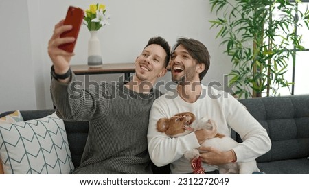 Two men couple making selfie by smartphone sitting on sofa with dog at home