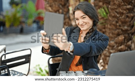 Young beautiful hispanic woman business worker make selfie by touchpad at coffee shop terrace