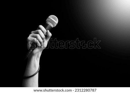 close up microphone in hand of singer raised his hand all the way up in live concert. singing concept. black and white Royalty-Free Stock Photo #2312280787