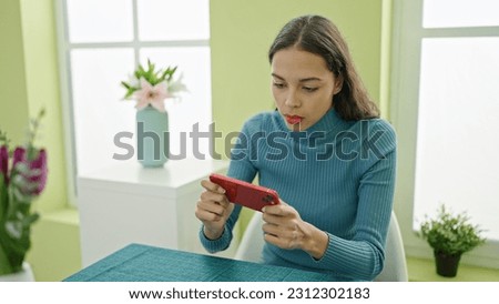 Young beautiful hispanic woman playing video game sitting on table at home