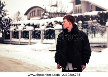Young blond man in black outwear near luxury villa, winter background