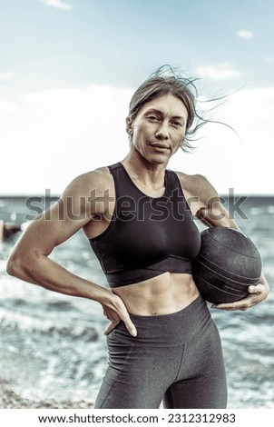 Muscular woman athlete in sportswear posing with medicine balls on the beach