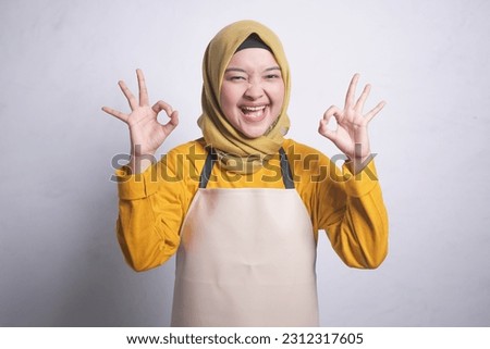 portrait of a beautiful Muslim woman wearing an orange shirt and apron she is opening her mouth and with her hands okay into a style isolated over white background
