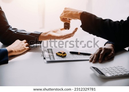 A car rental company employee is handing out the car keys to the renter after discussing the rental details and conditions together with the renter signing a car rental agreement. Concept car rental.