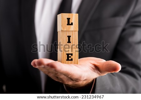 Businessman holding wooden alphabet blocks reading - Lie - balanced in the palm of his hand.