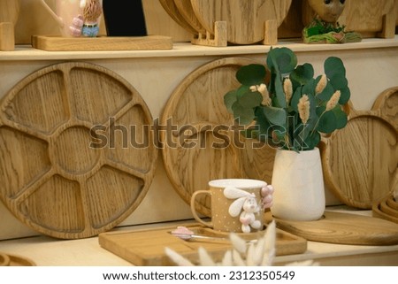 Close-up view of wooden trays with artificial flowers, bunny rabbit cup mug and cutting boards desks standing on eco shelf.

Household goods shop store. Kitchen utensils made of eco natural materials. Royalty-Free Stock Photo #2312350549