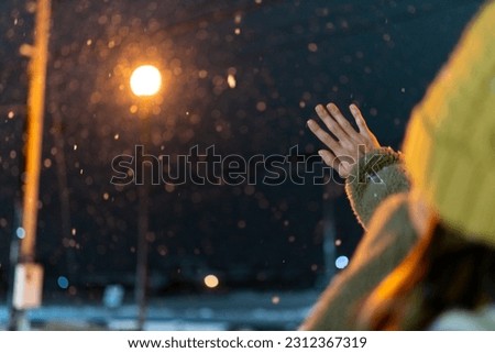 Young Asian woman in winter coat looking and playing beautiful snowflakes falling down during walking city street at night. Attractive girl enjoy and fun travel Japan on winter holiday vacation. Royalty-Free Stock Photo #2312367319