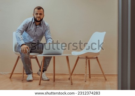 A confident businessman sitting and using laptop with a determined expression, while a beige background enhances the professional atmosphere, showcasing his productivity and expertise.