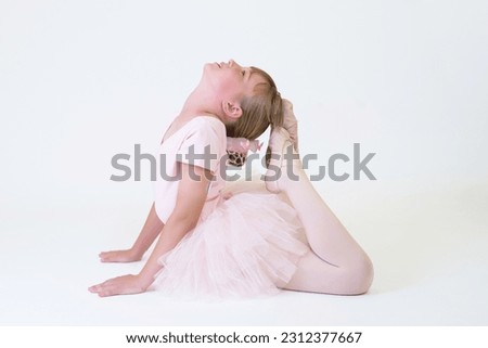 Little ballerina dancer in a pink tutu academy student posing on white background.
