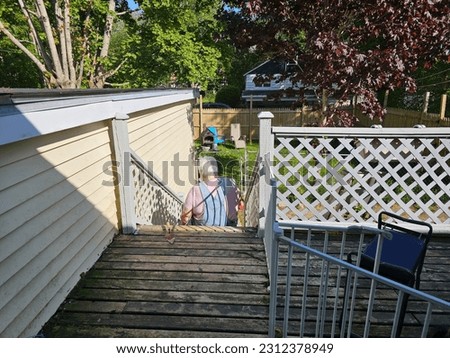 An elderly lady sitting on a staircase and painting the railings.