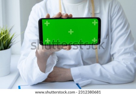 Green screen phone in horizontal position in medical clinic and doctor wearing uniform on the background. Blank and copy space smartphone. Health care, online medicine