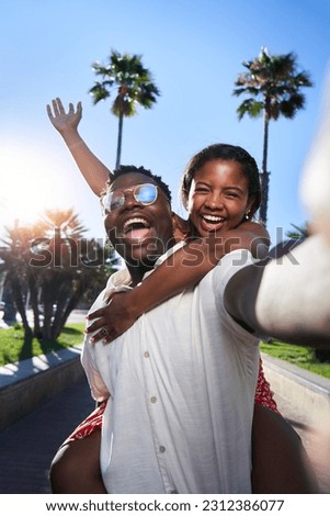 Cheerful selfie of a young African American couple on their summer vacation on an island. African man giving piggyback ride to his Latina girlfriend. Social media sharing. Royalty-Free Stock Photo #2312386077