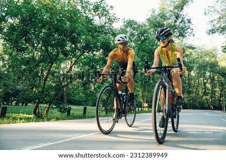 Smiling sporty couple on bicycles during weekend cycle ride while wearing sports clothes and helmets. Traveling by high-performance sport bicycles. Sports and healthy lifestyle. Copy space. Royalty-Free Stock Photo #2312389949