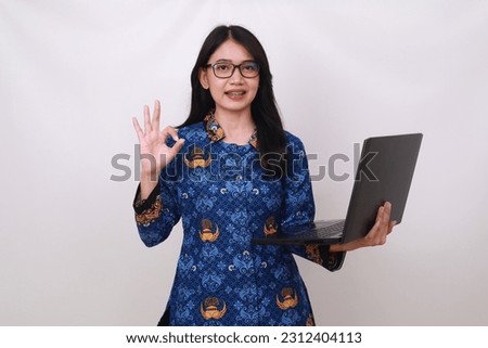 Asian female in batik korpri, indonesian traditional uniform holding laptop and making okay gesture Royalty-Free Stock Photo #2312404113