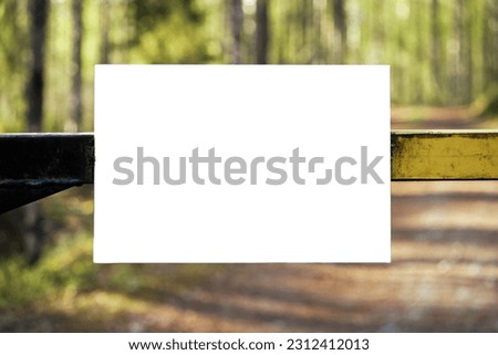 Empty white sign attached to a boom barrier in a forest road.